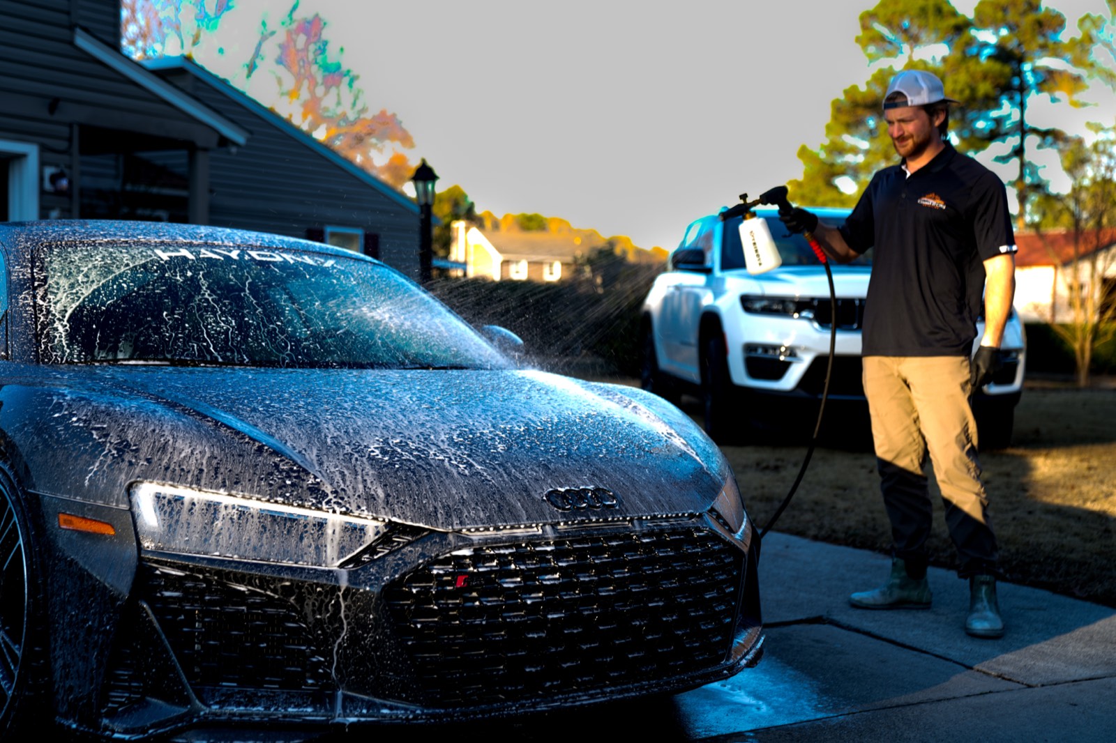 Detailer rinsing a foam-covered Audi R8 with a pressure washer in a driveway