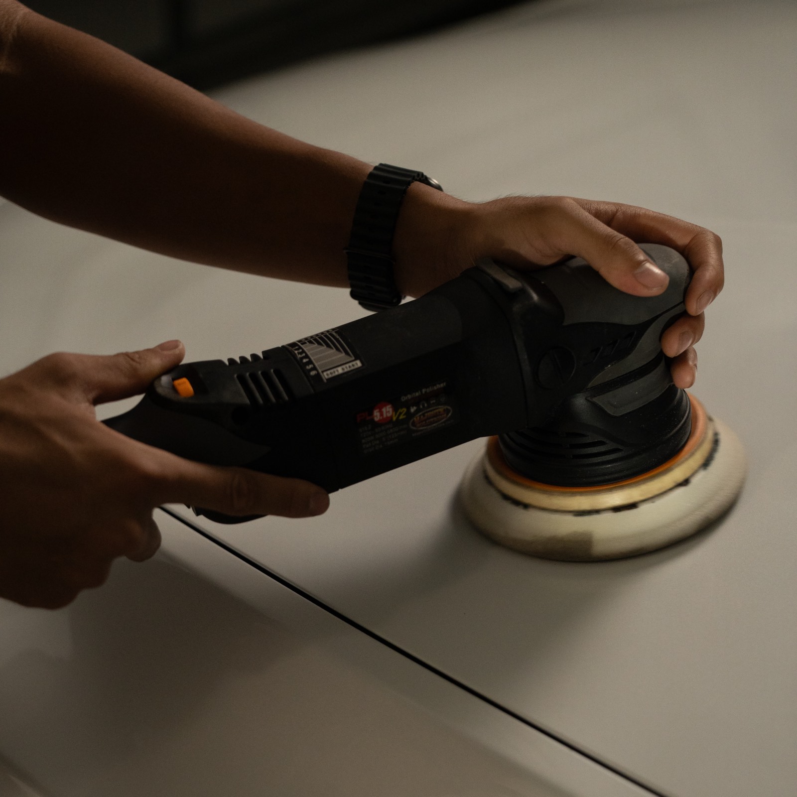 Close-up of a dual-action polisher performing paint correction on a white car panel