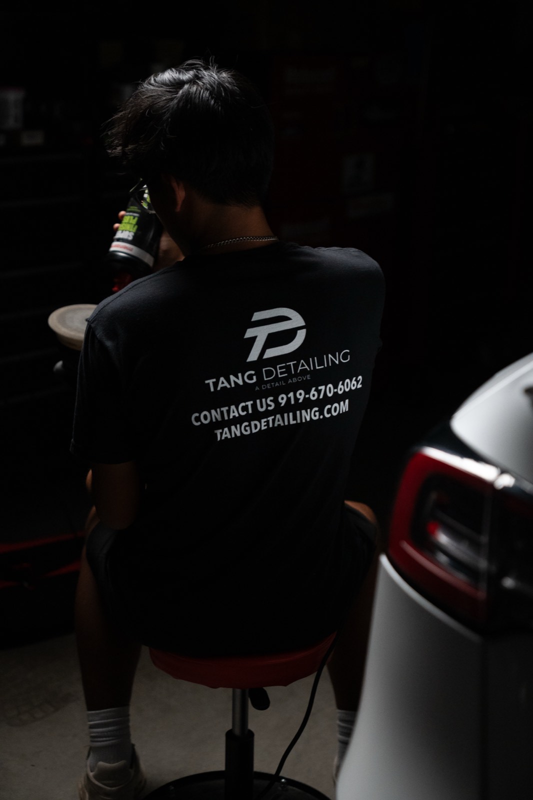 Auto detailer wearing branded shop apparel in a low-lit garage