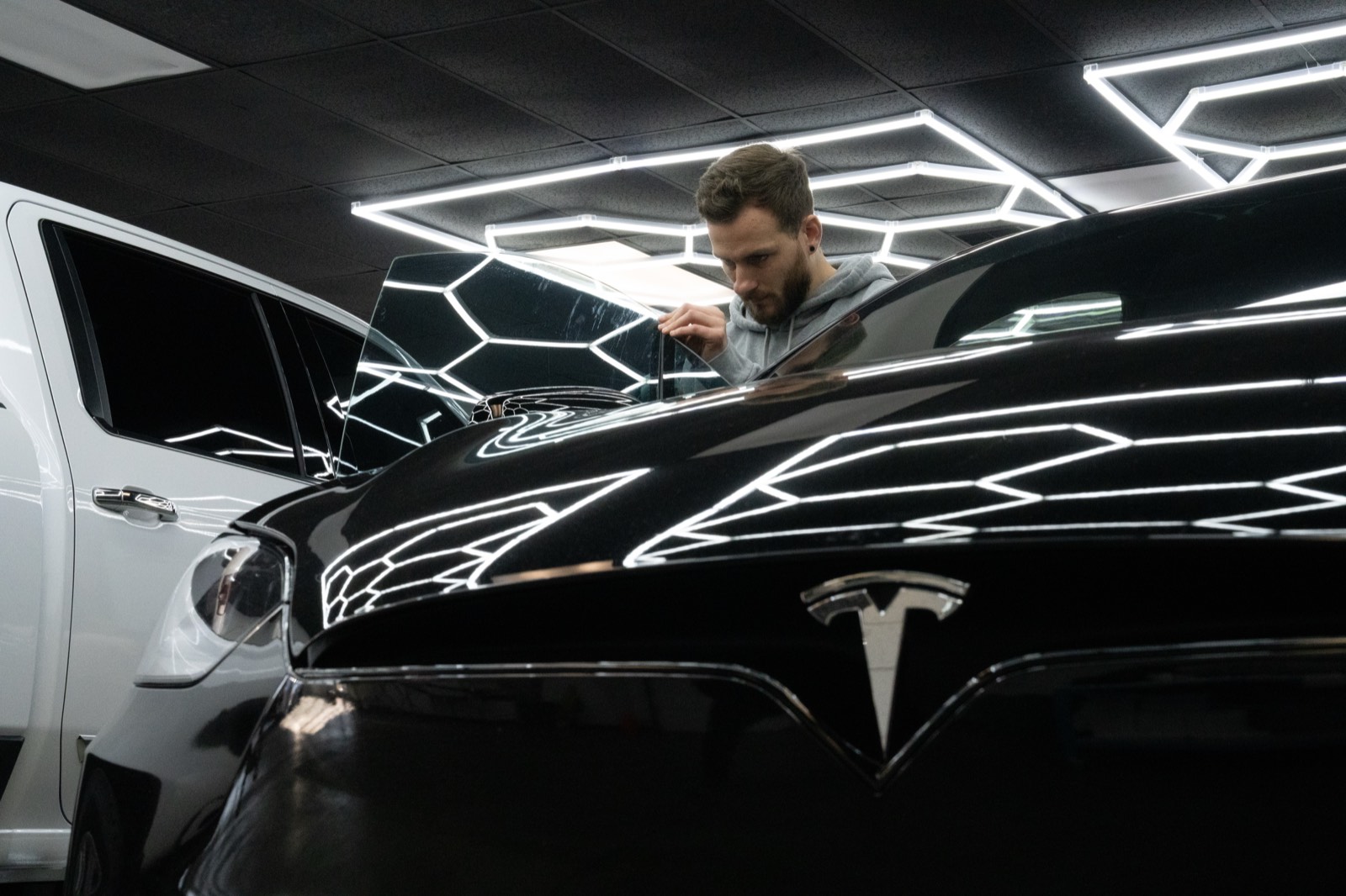 Detailer inspecting a glossy black Tesla under hexagon LED lighting in a professional detailing studio