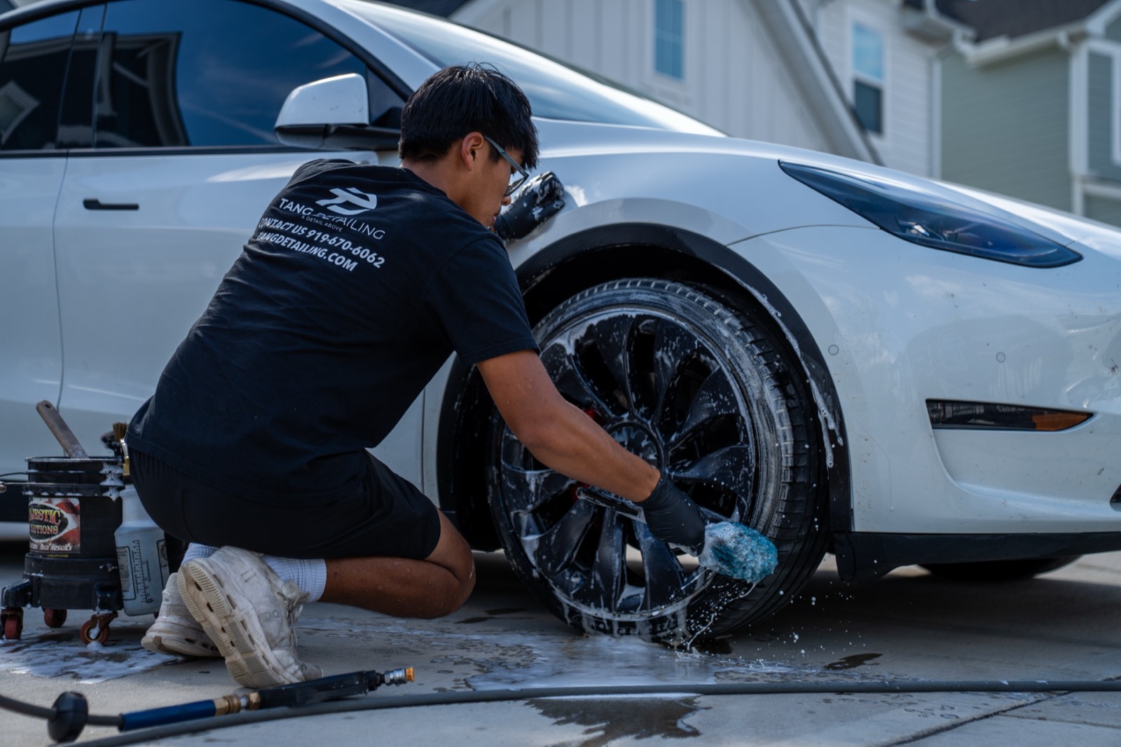 Detailer deep-cleaning a Tesla Model Y wheel and brake caliper by hand