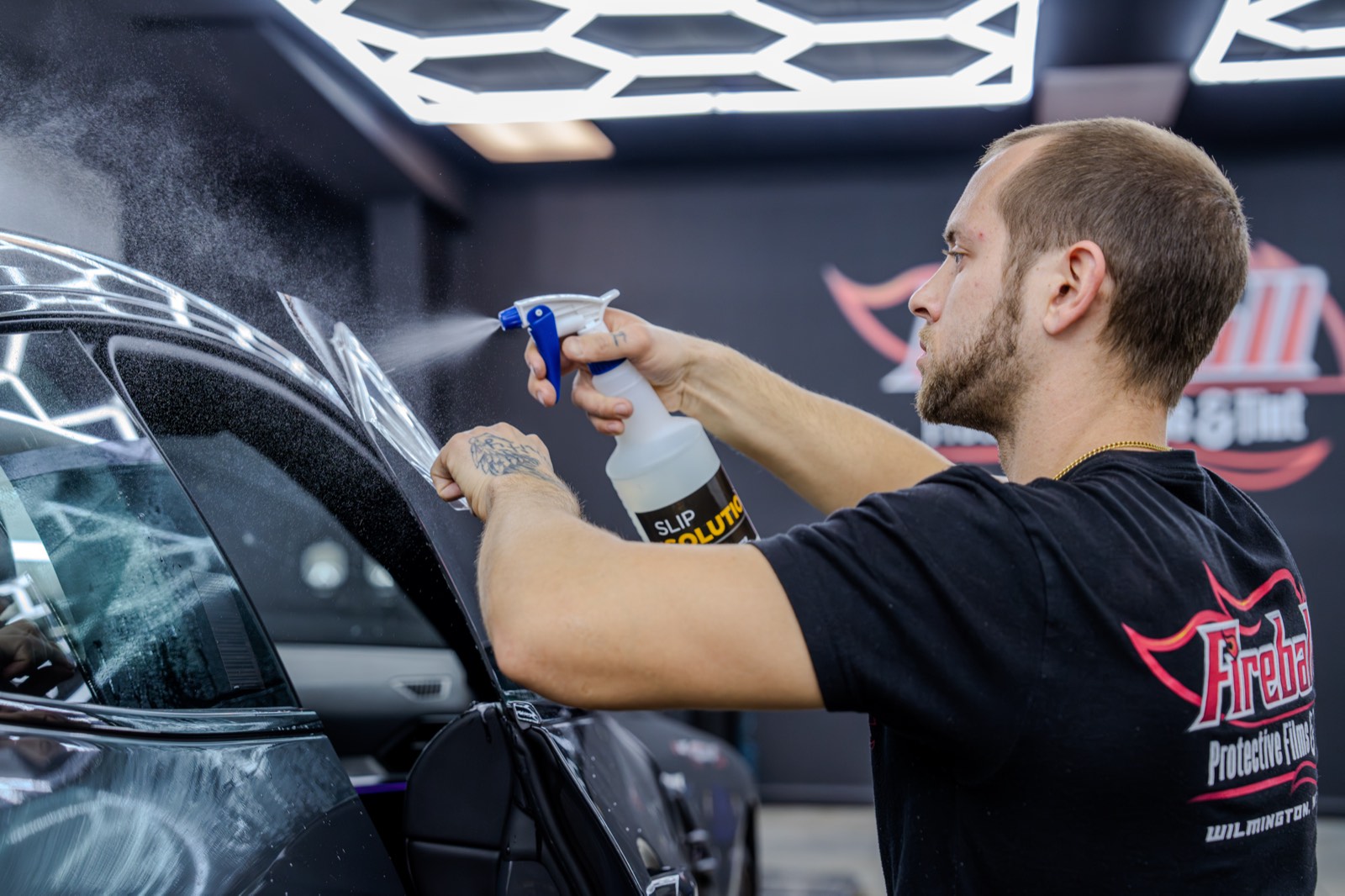 Technician spraying slip solution while installing window tint on a black car
